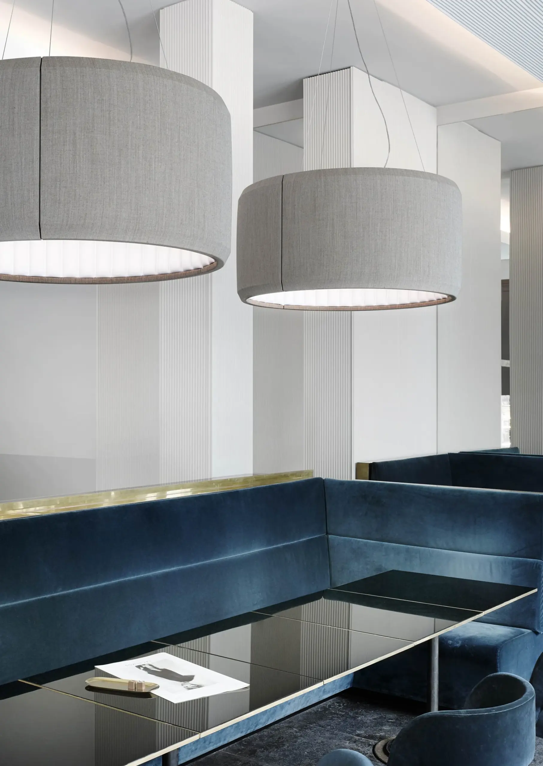 Zwei graue Luceplan Akustikpendelleuchten Silenzio über blauer Sitzbank im Restaurant