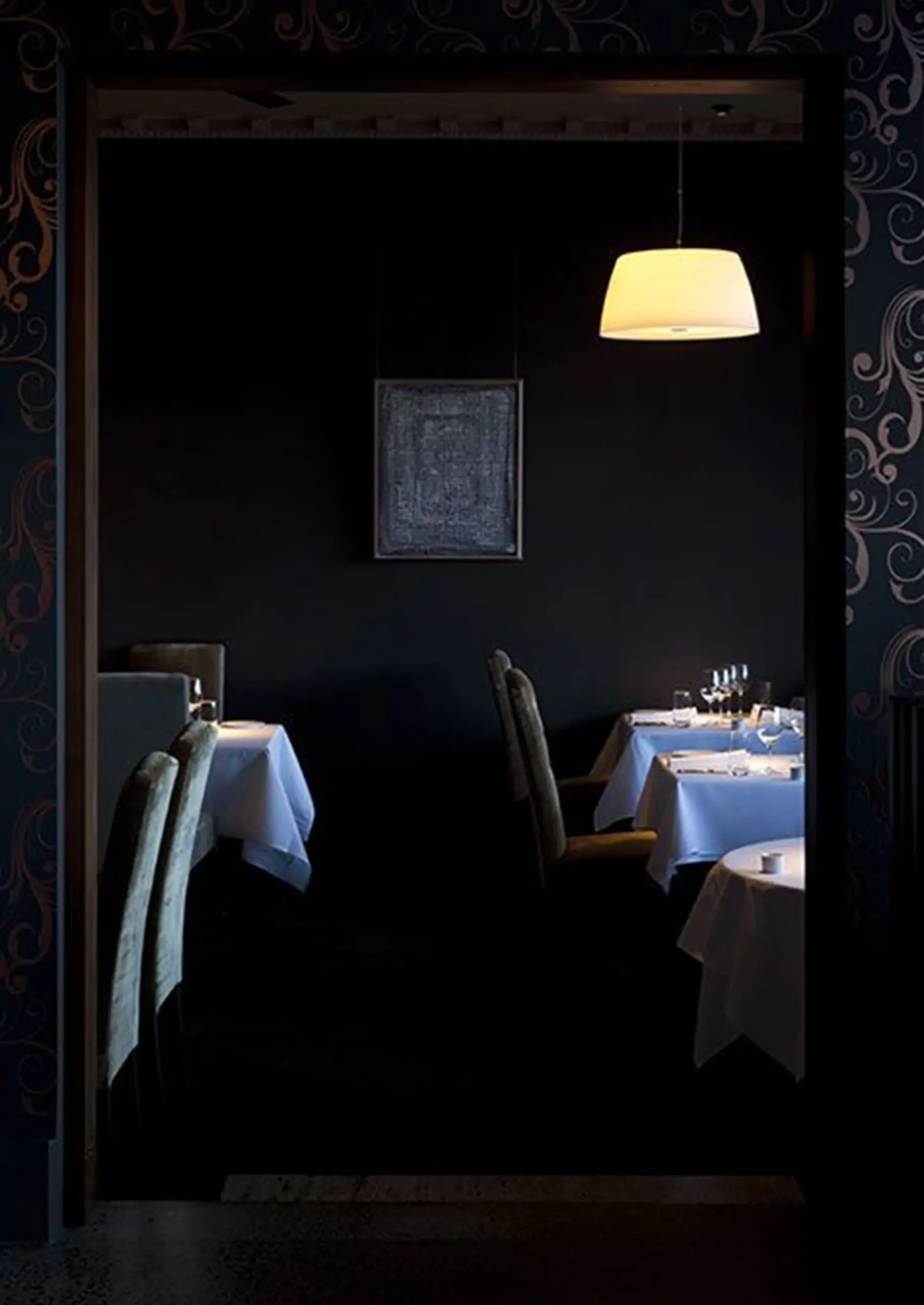 Warm leuchtende Prandina Pendelleuchte über gedeckten Tischen in einem dunklen Restaurant